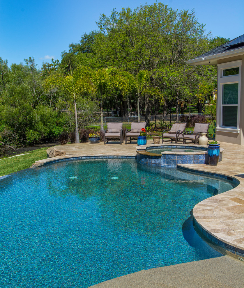 This is an example of a large traditional backyard kidney-shaped infinity pool in Tampa with a hot tub and natural stone pavers.