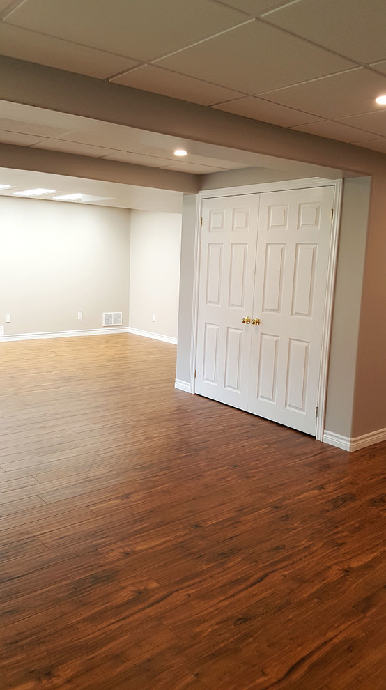 Example of a large transitional walk-out laminate floor and brown floor basement design in Toronto