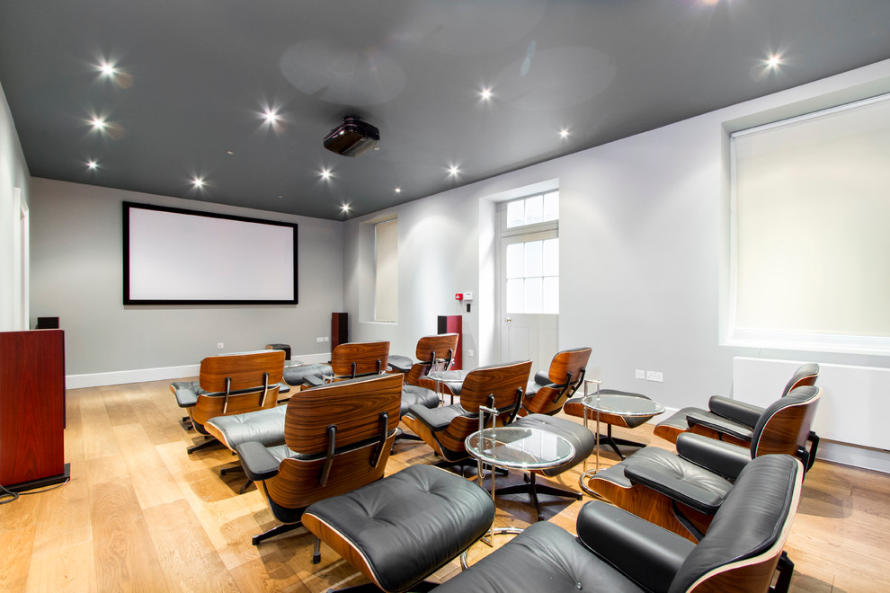 This is an example of a contemporary enclosed home theatre in London with white walls, light hardwood floors, a projector screen and yellow floor.
