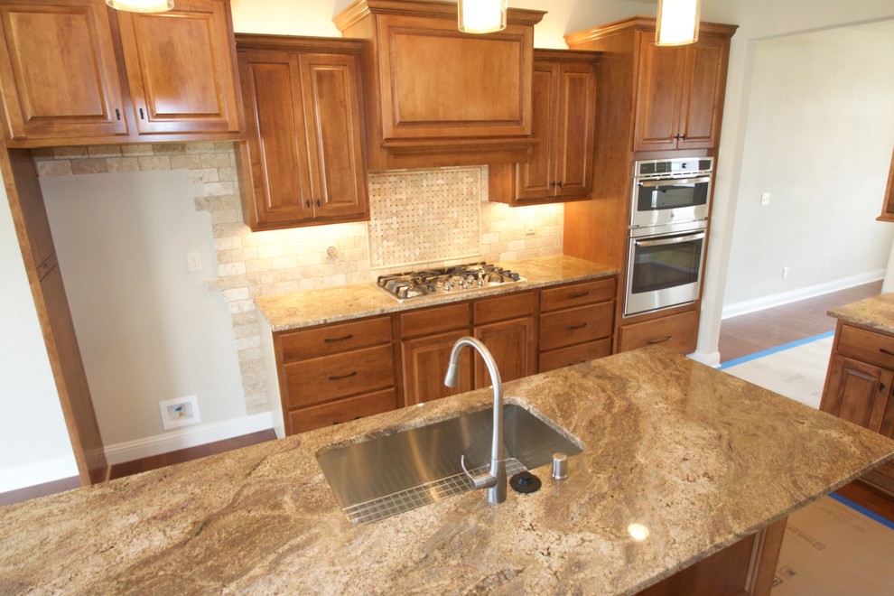 Example of a large transitional galley medium tone wood floor open concept kitchen design in Milwaukee with an undermount sink, raised-panel cabinets, medium tone wood cabinets, granite countertops, beige backsplash, stone tile backsplash, stainless steel appliances and an island