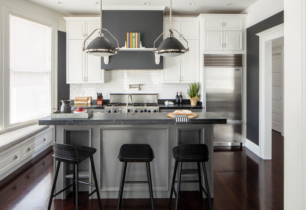 Design ideas for a transitional galley kitchen in San Francisco with raised-panel cabinets, white cabinets, white splashback, subway tile splashback, stainless steel appliances, dark hardwood floors, with island, brown floor and grey benchtop.
