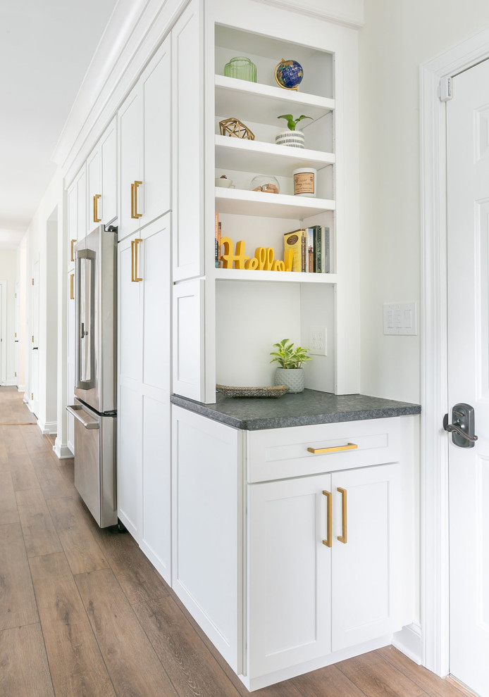 This is an example of a large classic l-shaped kitchen pantry in Baltimore with a built-in sink, shaker cabinets, white cabinets, engineered stone countertops, white splashback, ceramic splashback, stainless steel appliances, an island, brown floors and white worktops.