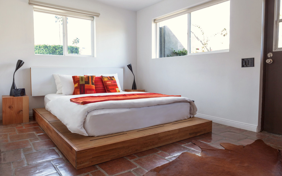 This is an example of a mid-sized guest bedroom in Los Angeles with white walls, terra-cotta floors and no fireplace.