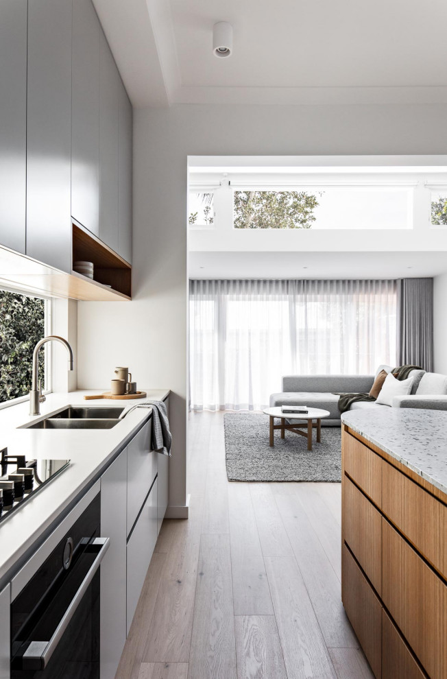 This is an example of a small contemporary galley eat-in kitchen in Sydney with a double-bowl sink, grey cabinets, terrazzo benchtops, black appliances, light hardwood floors, with island and grey benchtop.