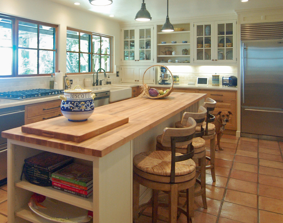 This is an example of a large mediterranean l-shaped separate kitchen in San Luis Obispo with a farmhouse sink, beaded inset cabinets, white cabinets, marble benchtops, white splashback, stone tile splashback, stainless steel appliances, terra-cotta floors and with island.