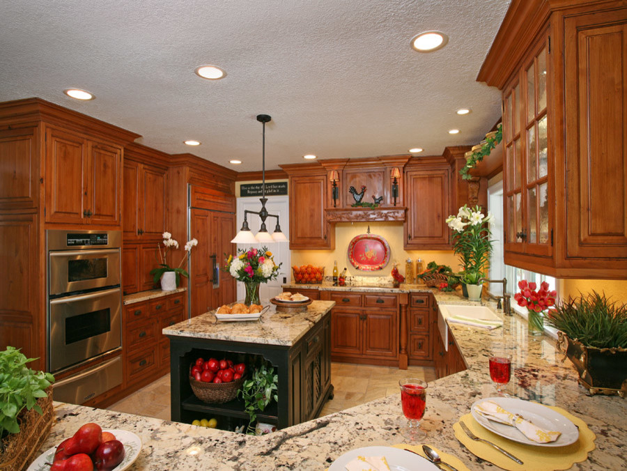 Enclosed kitchen - mid-sized rustic u-shaped travertine floor enclosed kitchen idea in Miami with a farmhouse sink, raised-panel cabinets, medium tone wood cabinets, granite countertops, yellow backsplash, stainless steel appliances and an island