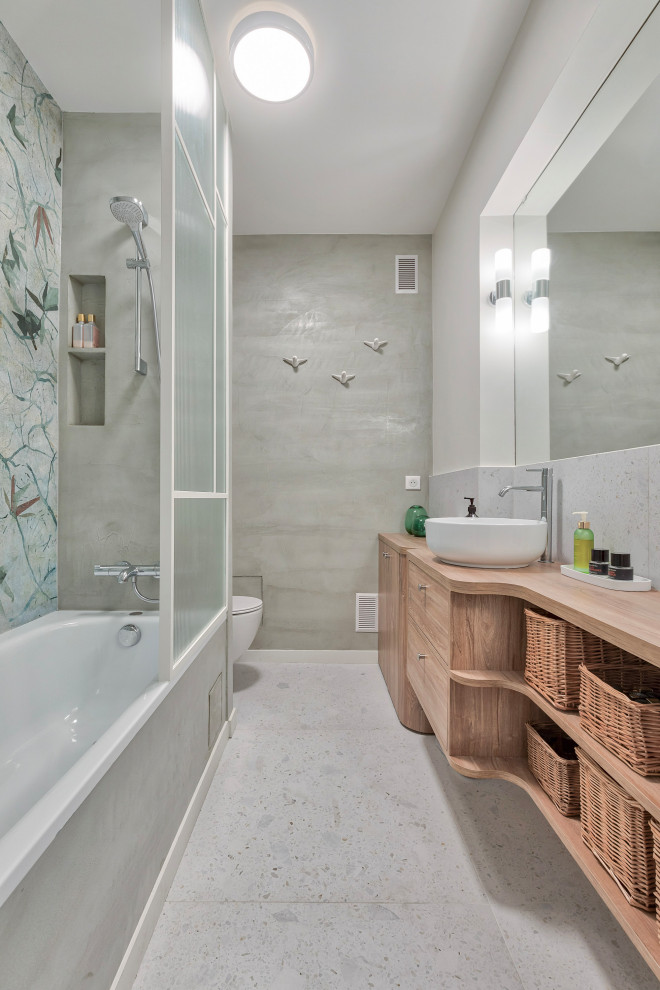 Exemple d'une salle de bain principale moderne en bois clair de taille moyenne avec un placard à porte affleurante, une baignoire encastrée, un combiné douche/baignoire, WC suspendus, un carrelage gris, un mur gris, un sol en terrazzo, un lavabo posé, un plan de toilette en bois, un sol gris, un plan de toilette marron, une niche, meuble simple vasque, meuble-lavabo suspendu et du papier peint.