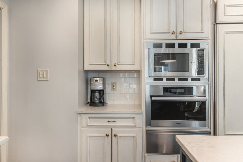 Example of a transitional medium tone wood floor and brown floor kitchen design in DC Metro with an undermount sink, recessed-panel cabinets, white cabinets, granite countertops, white backsplash, subway tile backsplash, stainless steel appliances, an island and white countertops