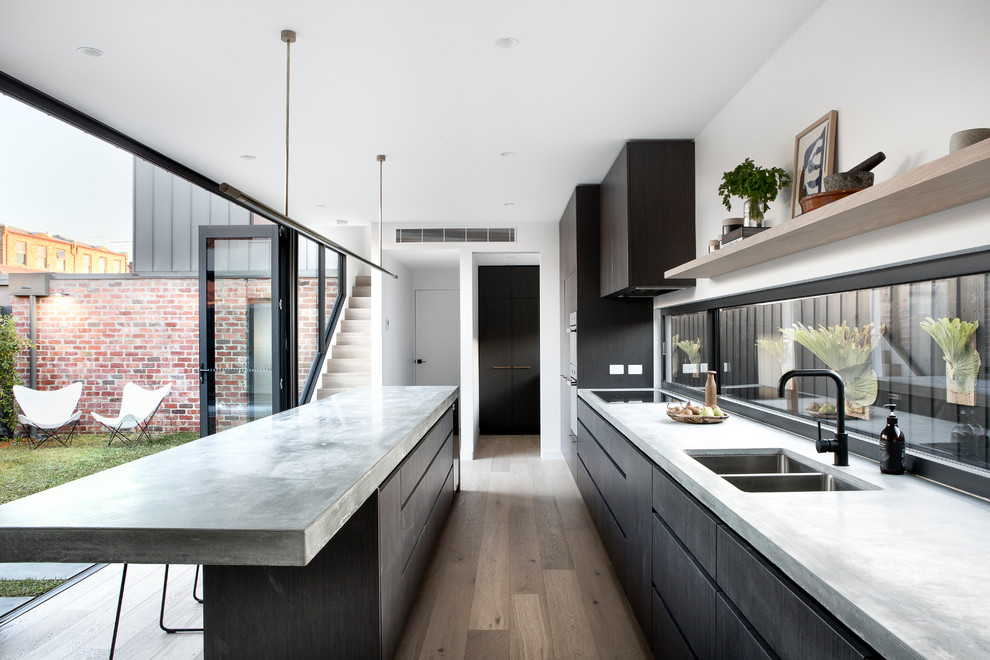 Modern galley eat-in kitchen in Melbourne with a double-bowl sink, dark wood cabinets, concrete benchtops, light hardwood floors and with island.