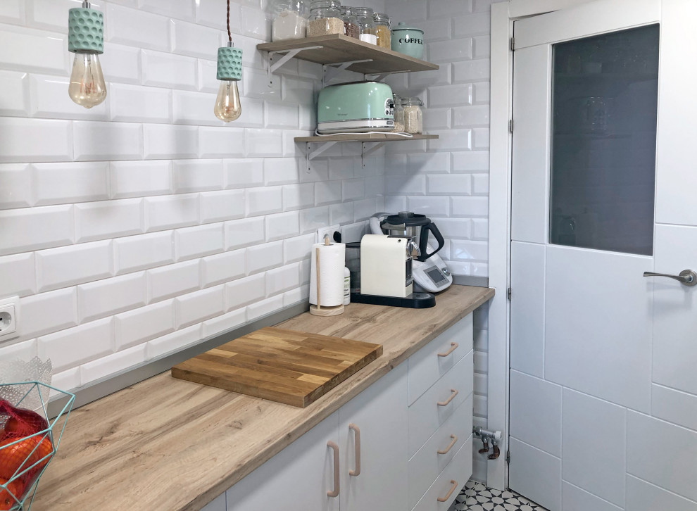 Small scandinavian separate kitchen in Madrid with an undermount sink, flat-panel cabinets, white cabinets, wood benchtops, metallic splashback, metal splashback, stainless steel appliances, ceramic floors, no island, multi-coloured floor and brown benchtop.