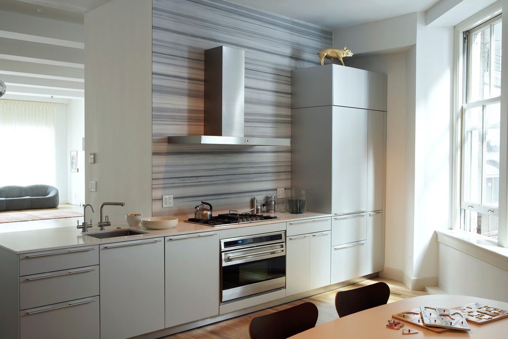 Small contemporary single-wall eat-in kitchen in New York with flat-panel cabinets, grey cabinets, no island, an undermount sink, multi-coloured splashback, stainless steel appliances and light hardwood floors.