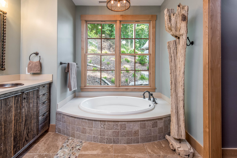 Large country master bathroom in Other with flat-panel cabinets, dark wood cabinets, a drop-in tub, a corner shower, brown tile, stone slab, grey walls, a drop-in sink, solid surface benchtops, brown floor, a hinged shower door and grey benchtops.