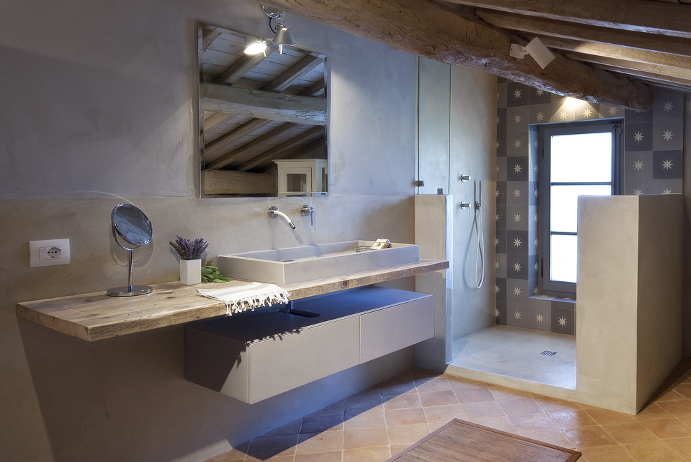 This is an example of a mid-sized country 3/4 bathroom in Rome with flat-panel cabinets, white cabinets, a corner shower, gray tile, terra-cotta floors, a trough sink, wood benchtops, an open shower and beige benchtops.