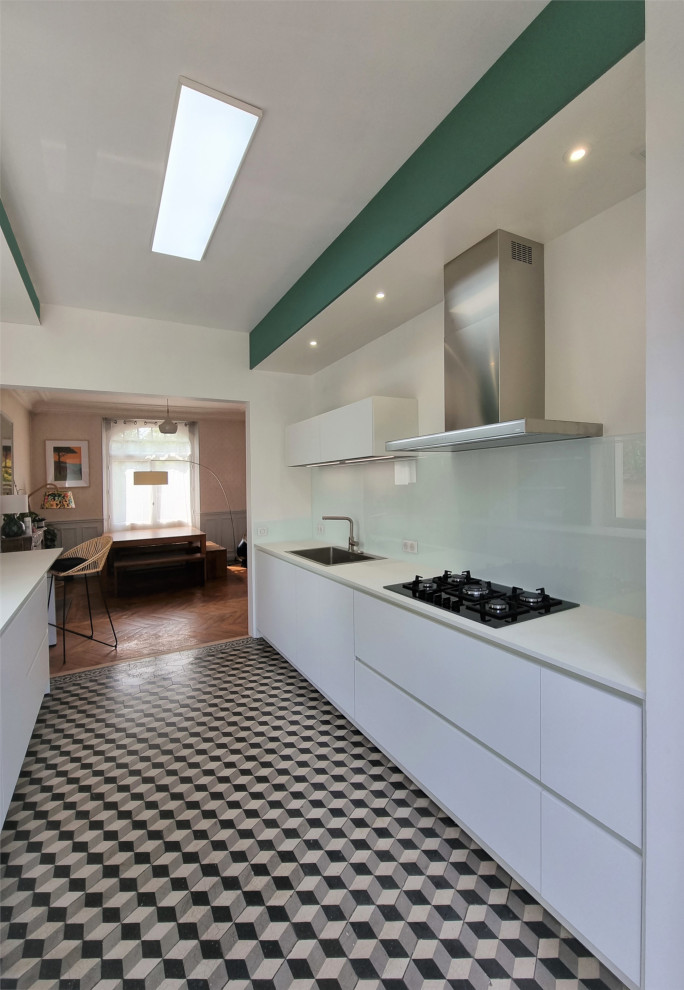 Photo of an expansive modern galley open plan kitchen in Other with an integrated sink, flat-panel cabinets, white cabinets, wood benchtops, white splashback, glass tile splashback, panelled appliances, cement tiles, no island, multi-coloured floor and white benchtop.