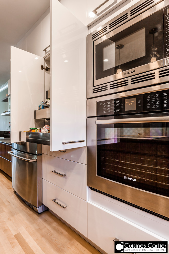 Large transitional galley medium tone wood floor eat-in kitchen photo in Montreal with an undermount sink, flat-panel cabinets, dark wood cabinets, quartzite countertops, white backsplash, mosaic tile backsplash, stainless steel appliances and an island
