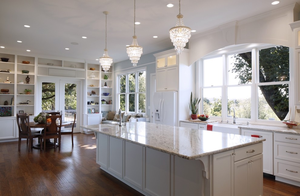 Inspiration for an expansive traditional eat-in kitchen in Portland with a farmhouse sink, recessed-panel cabinets, white cabinets, marble benchtops, white splashback, subway tile splashback, white appliances, medium hardwood floors and with island.