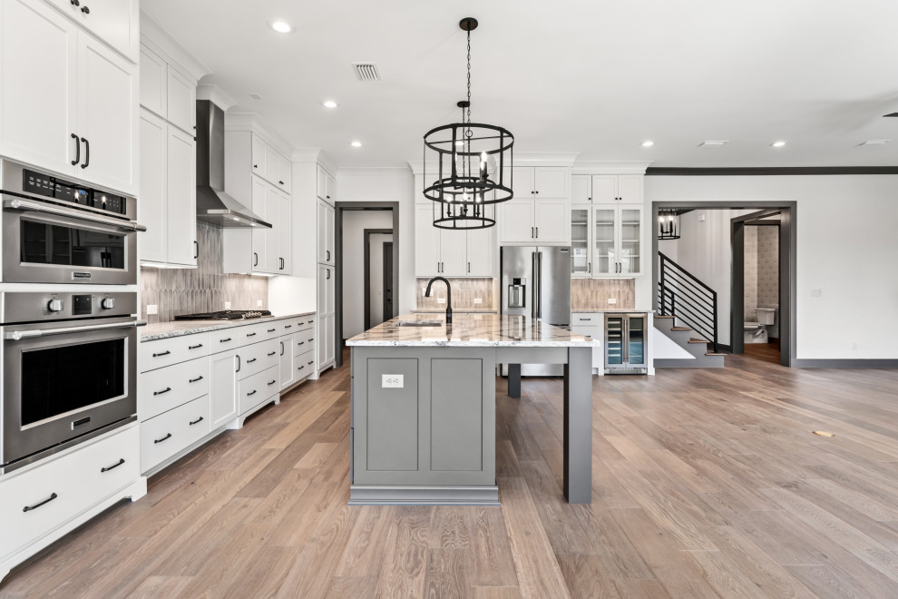 Example of a mid-sized transitional l-shaped medium tone wood floor and brown floor open concept kitchen design with recessed-panel cabinets, white cabinets, quartz countertops, ceramic backsplash, stainless steel appliances and an island