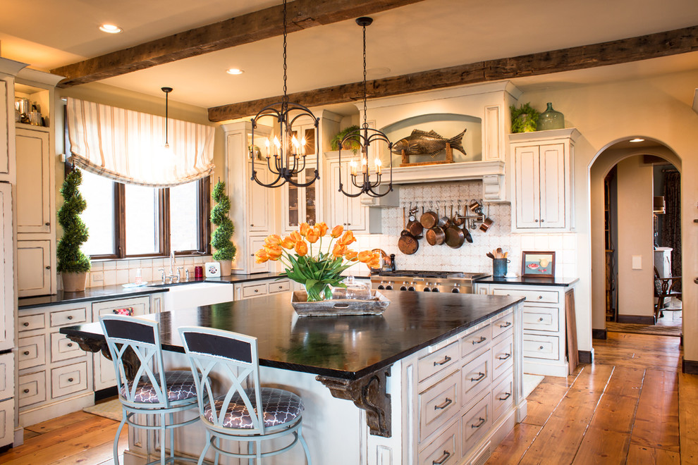 Inspiration for a large rustic l-shaped medium tone wood floor eat-in kitchen remodel in Oklahoma City with a farmhouse sink, distressed cabinets, soapstone countertops, terra-cotta backsplash, stainless steel appliances, recessed-panel cabinets, white backsplash and an island