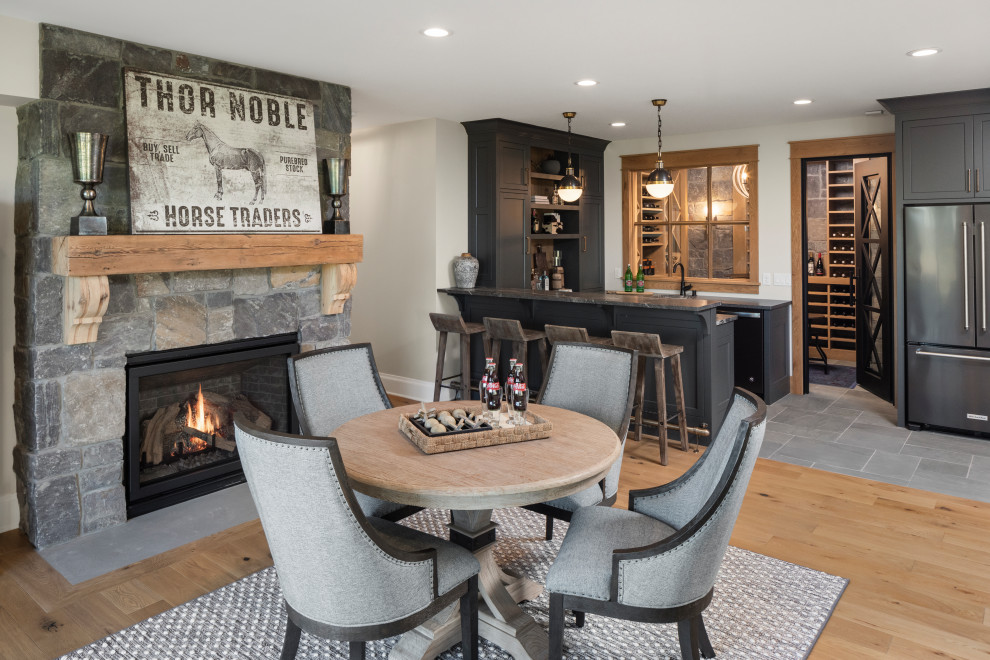 This is an example of a country basement in Minneapolis with slate floors, blue floor, a game room, a home bar, white walls, a standard fireplace and a stone fireplace surround.