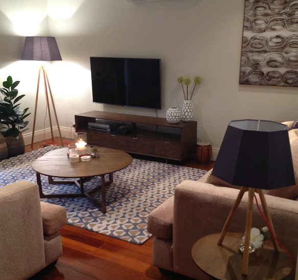 This is an example of a mid-sized contemporary open concept living room in Melbourne with beige walls, medium hardwood floors, a freestanding tv and brown floor.