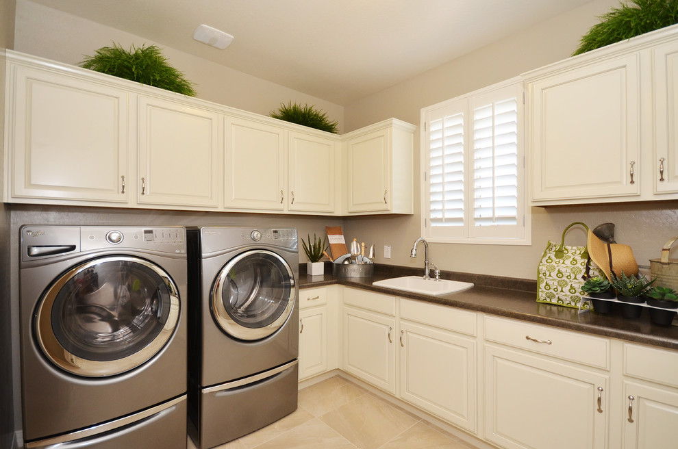 Photo of a mid-sized traditional l-shaped utility room in Phoenix with a drop-in sink, raised-panel cabinets, white cabinets, laminate benchtops, beige walls, ceramic floors, a side-by-side washer and dryer and beige floor.