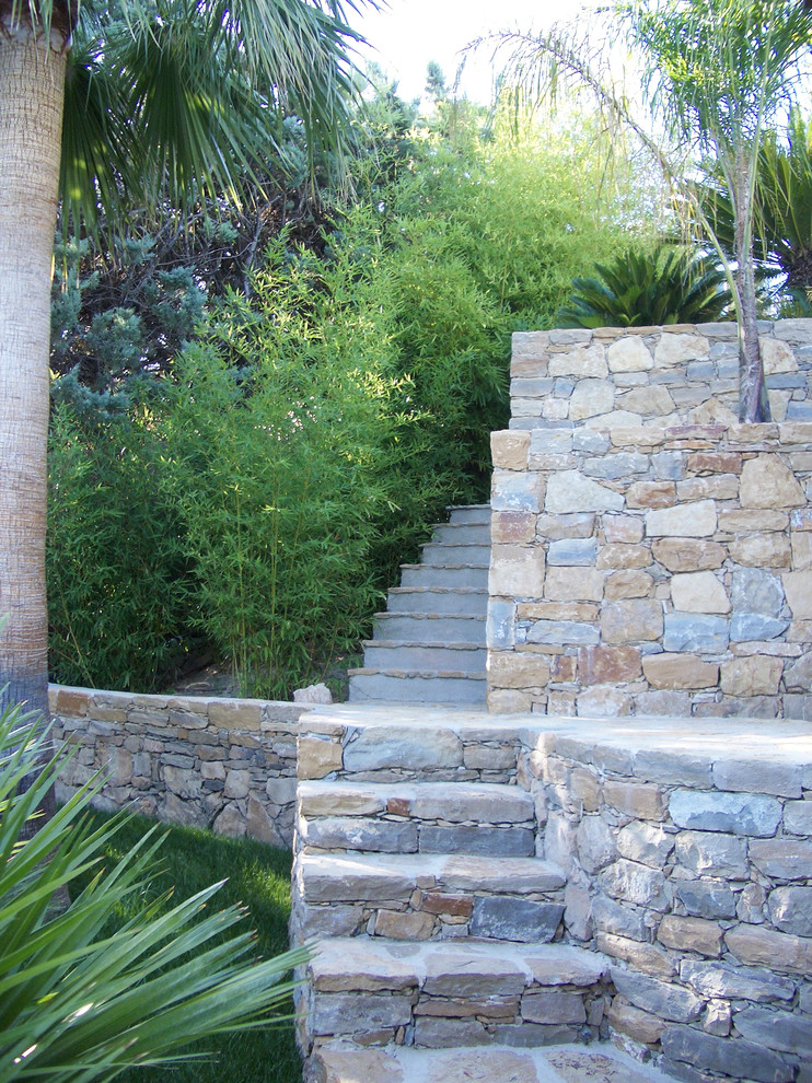 This is an example of a large tropical backyard shaded garden for summer in Marseille with a garden path and natural stone pavers.