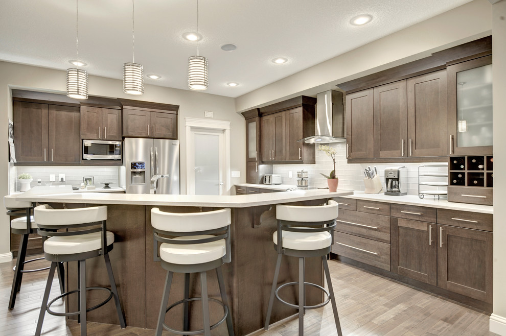Inspiration for a large transitional l-shaped eat-in kitchen in Edmonton with an undermount sink, raised-panel cabinets, medium wood cabinets, quartzite benchtops, beige splashback, ceramic splashback, stainless steel appliances, medium hardwood floors and with island.