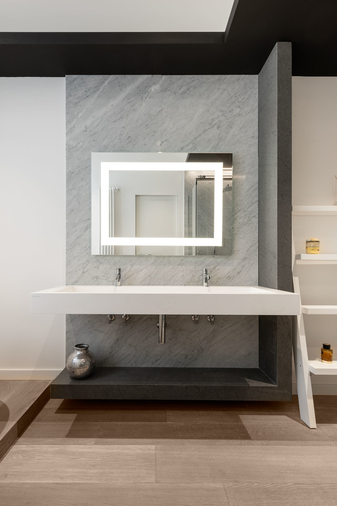 Photo of a mid-sized contemporary master bathroom in Rome with open cabinets, gray tile, stone slab, white walls, light hardwood floors, a wall-mount sink, solid surface benchtops, white benchtops and brown floor.