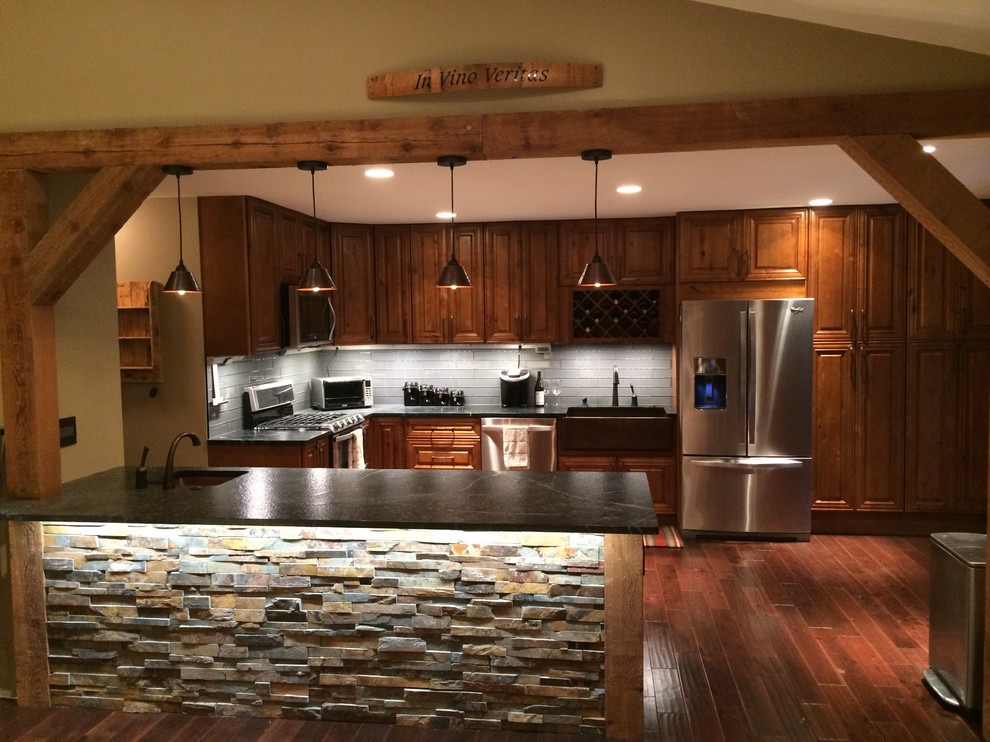 Inspiration for a large rustic l-shaped medium tone wood floor eat-in kitchen remodel in St Louis with a farmhouse sink, raised-panel cabinets, granite countertops, gray backsplash, glass tile backsplash, stainless steel appliances and a peninsula
