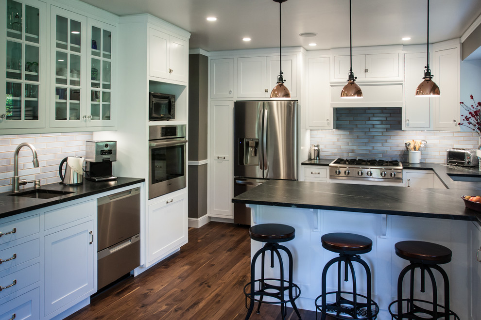 This is an example of a traditional eat-in kitchen in San Francisco with shaker cabinets, white cabinets, soapstone benchtops, blue splashback, ceramic splashback, stainless steel appliances, medium hardwood floors and a peninsula.