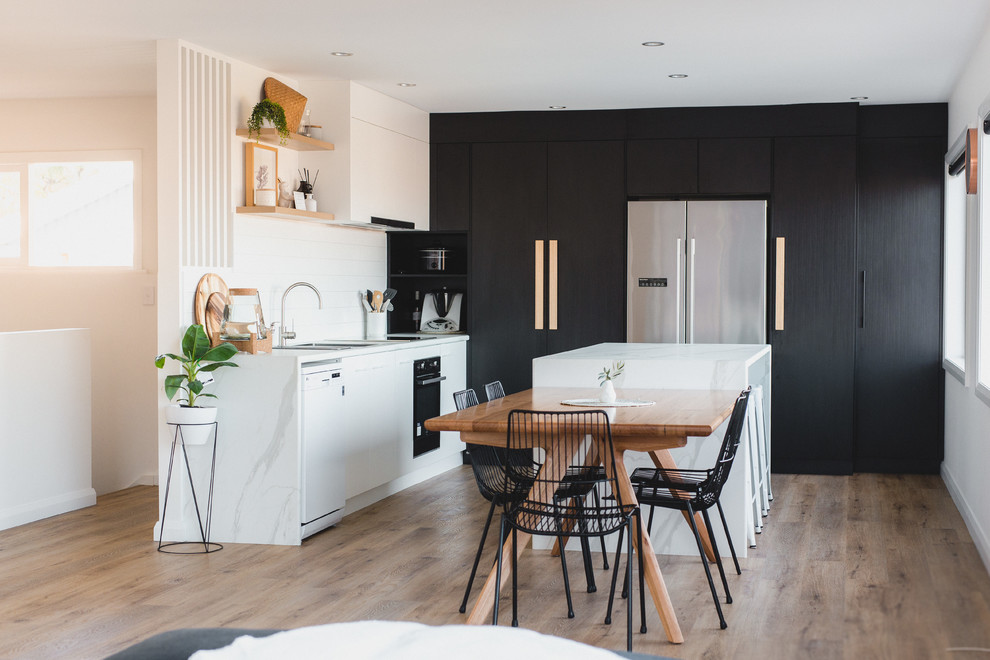 Contemporary l-shaped eat-in kitchen in Hobart with an undermount sink, flat-panel cabinets, black cabinets, white splashback, stainless steel appliances, medium hardwood floors, with island, brown floor and white benchtop.