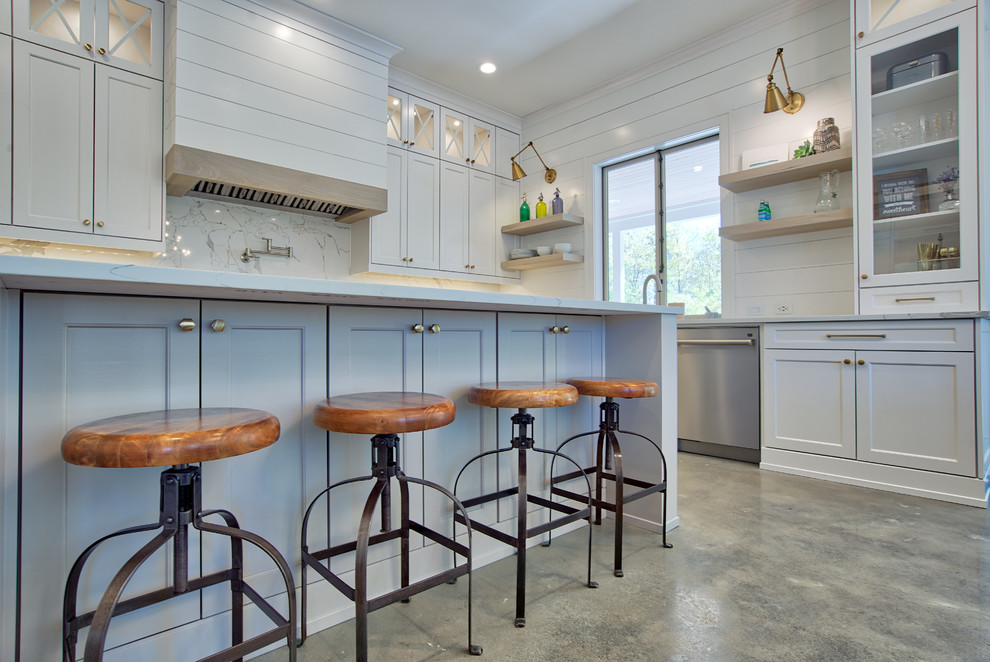 This is an example of a large country u-shaped eat-in kitchen in Atlanta with a farmhouse sink, shaker cabinets, white cabinets, quartz benchtops, white splashback, stone slab splashback, stainless steel appliances, concrete floors, with island, grey floor and white benchtop.