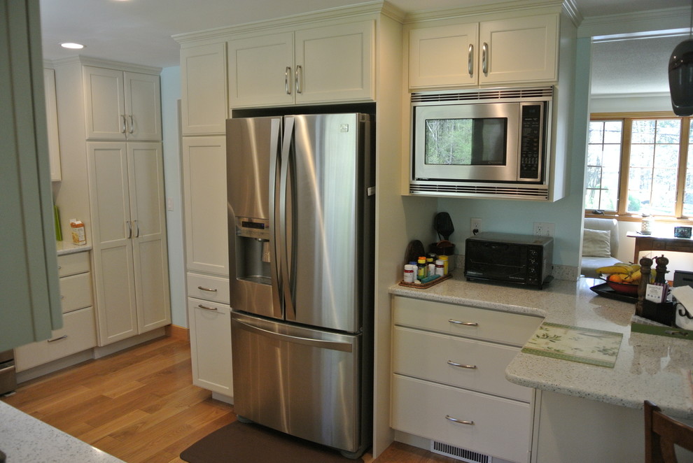 Example of a transitional l-shaped medium tone wood floor eat-in kitchen design in Boston with an undermount sink, shaker cabinets, white cabinets, recycled glass countertops, white backsplash, subway tile backsplash, stainless steel appliances, a peninsula and white countertops