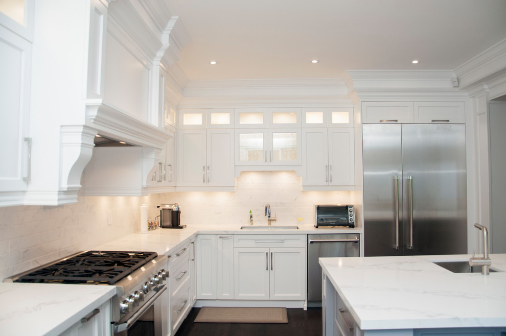Large transitional l-shaped dark wood floor and brown floor enclosed kitchen photo in Toronto with an undermount sink, shaker cabinets, white cabinets, quartz countertops, white backsplash, marble backsplash, stainless steel appliances, an island and white countertops