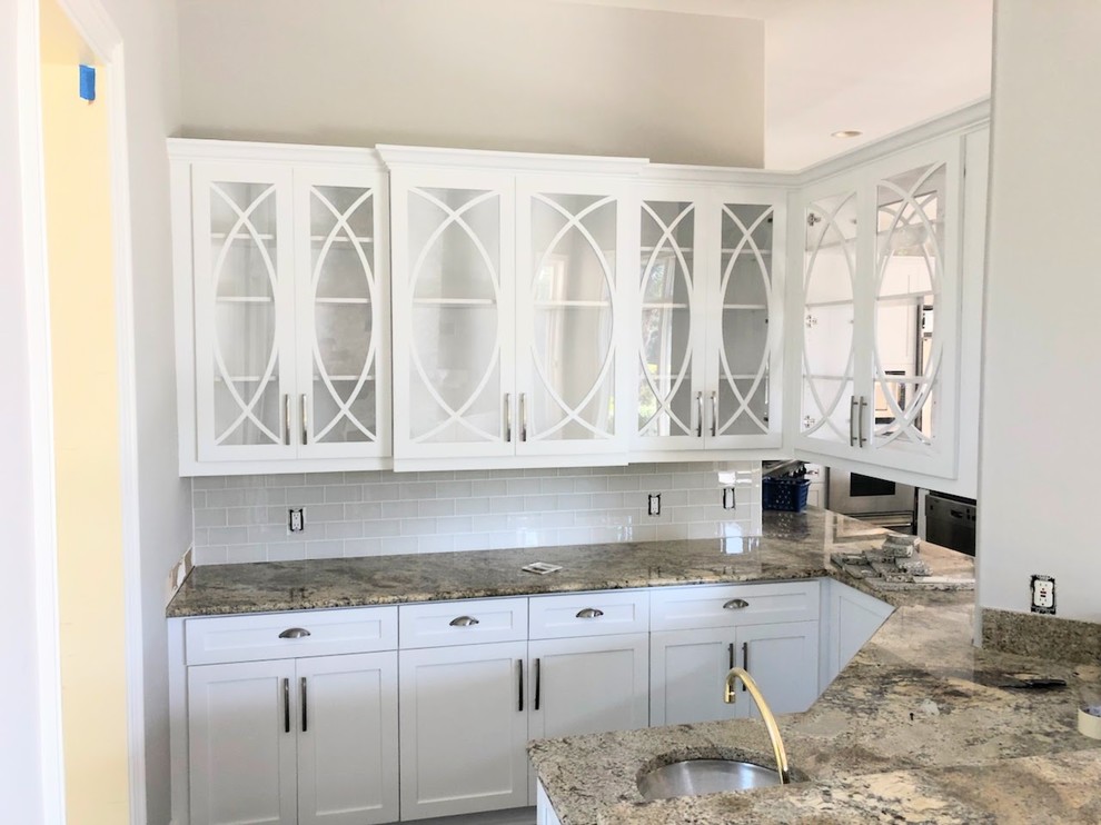 Open concept kitchen - mid-sized transitional porcelain tile and brown floor open concept kitchen idea with a farmhouse sink, shaker cabinets, white cabinets, granite countertops, white backsplash, ceramic backsplash, stainless steel appliances and an island