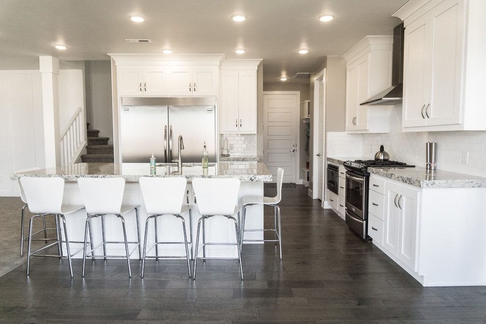 Open concept kitchen - mid-sized l-shaped dark wood floor and brown floor open concept kitchen idea with a drop-in sink, shaker cabinets, white cabinets, granite countertops, white backsplash, subway tile backsplash, stainless steel appliances and an island