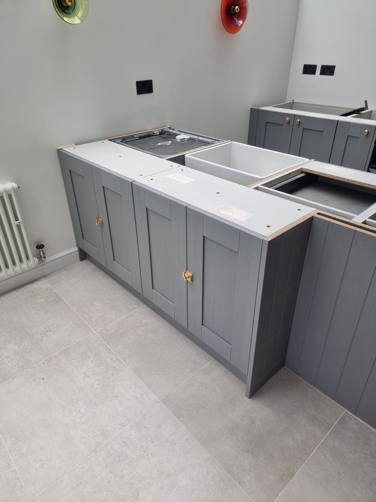 Large traditional single-wall kitchen in London with a belfast sink, shaker cabinets, grey cabinets, quartz worktops, integrated appliances, porcelain flooring, an island and white worktops.