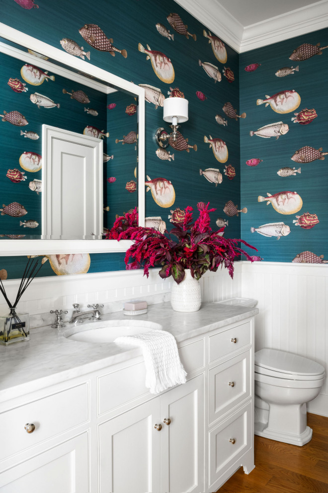 Beach style powder room in DC Metro with beaded inset cabinets, white cabinets, multi-coloured walls, medium hardwood floors, an undermount sink, brown floor, grey benchtops, a built-in vanity, decorative wall panelling and wallpaper.