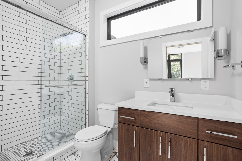 Photo of a mid-sized modern kids bathroom in Indianapolis with flat-panel cabinets, brown cabinets, a double shower, a one-piece toilet, white tile, subway tile, grey walls, ceramic floors, an undermount sink, marble benchtops, white floor, a sliding shower screen, white benchtops, a niche, a single vanity and a built-in vanity.