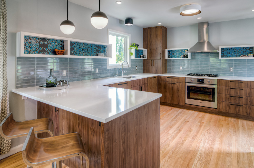 Inspiration for a contemporary u-shaped kitchen in Portland with an undermount sink, flat-panel cabinets, dark wood cabinets, grey splashback, stainless steel appliances, medium hardwood floors, a peninsula, brown floor and white benchtop.