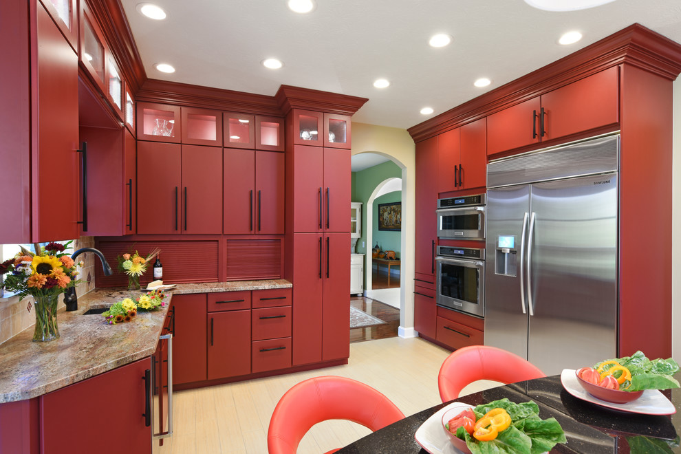 Example of a large transitional porcelain tile and beige floor enclosed kitchen design with an undermount sink, flat-panel cabinets, red cabinets, granite countertops, beige backsplash, travertine backsplash, stainless steel appliances and an island