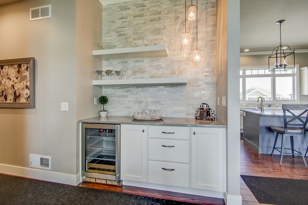 Inspiration for a large transitional l-shaped medium tone wood floor kitchen remodel with a farmhouse sink, recessed-panel cabinets, white cabinets, stone tile backsplash, stainless steel appliances and an island