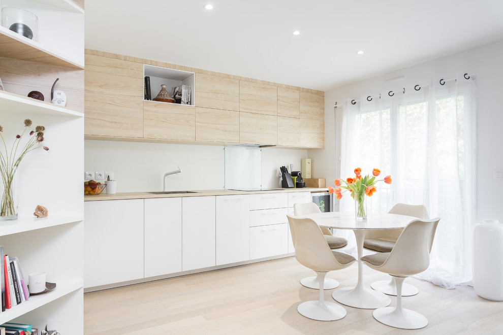 Inspiration for a mid-sized scandinavian single-wall eat-in kitchen in Paris with flat-panel cabinets, white cabinets, laminate benchtops, white splashback, glass sheet splashback, no island, an undermount sink, panelled appliances, light hardwood floors, beige floor and beige benchtop.