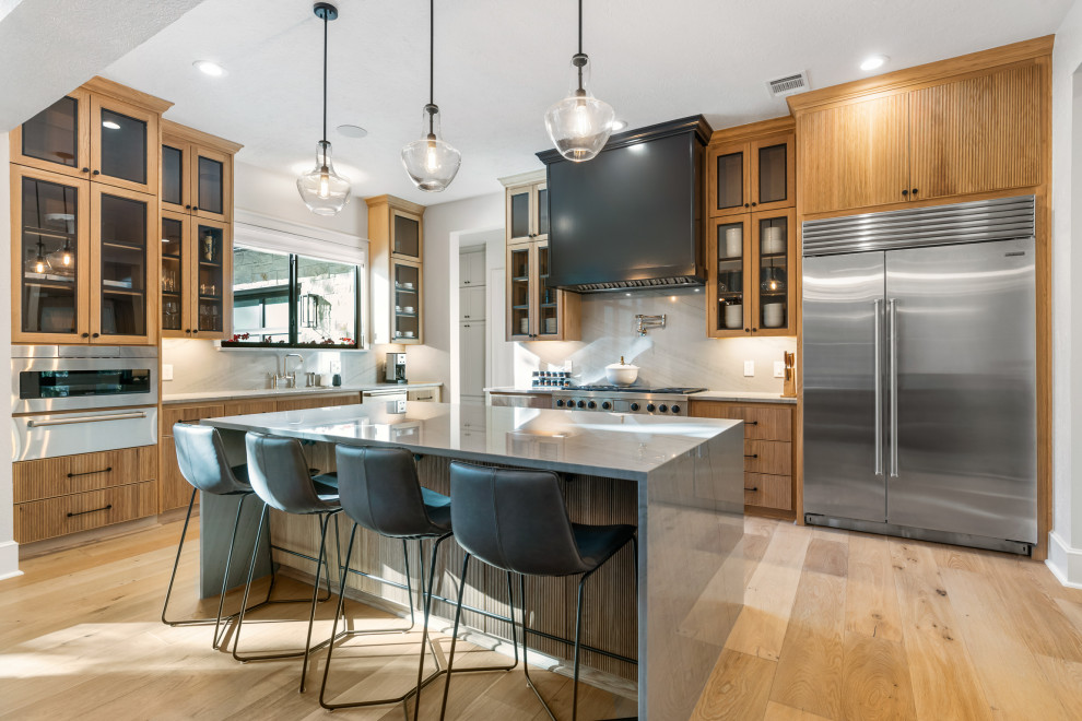 Design ideas for a large transitional l-shaped eat-in kitchen in Houston with an undermount sink, glass-front cabinets, medium wood cabinets, quartz benchtops, beige splashback, stone slab splashback, stainless steel appliances, medium hardwood floors, with island and grey benchtop.