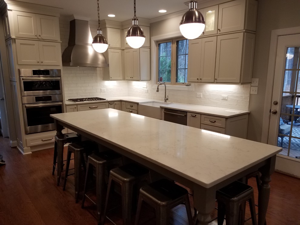 Photo of a mid-sized modern l-shaped open plan kitchen in Raleigh with an undermount sink, raised-panel cabinets, brown cabinets, granite benchtops, beige splashback, travertine splashback, black appliances and with island.