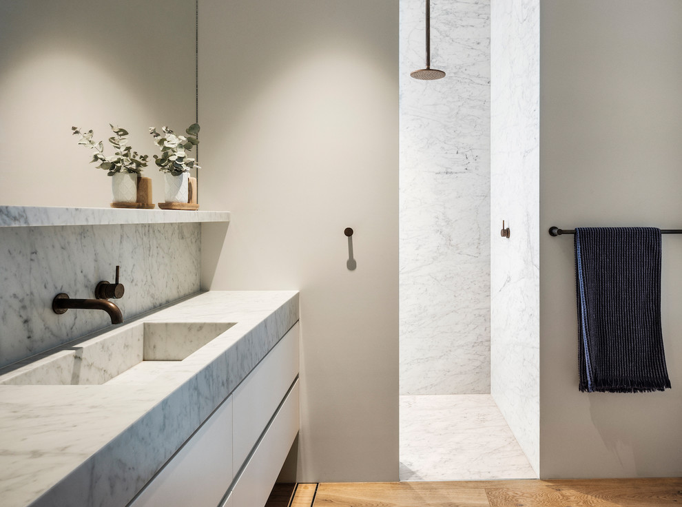This is an example of a contemporary bathroom in Sydney with flat-panel cabinets, white cabinets, a curbless shower, white tile, white walls, medium hardwood floors, an integrated sink, brown floor, an open shower and white benchtops.