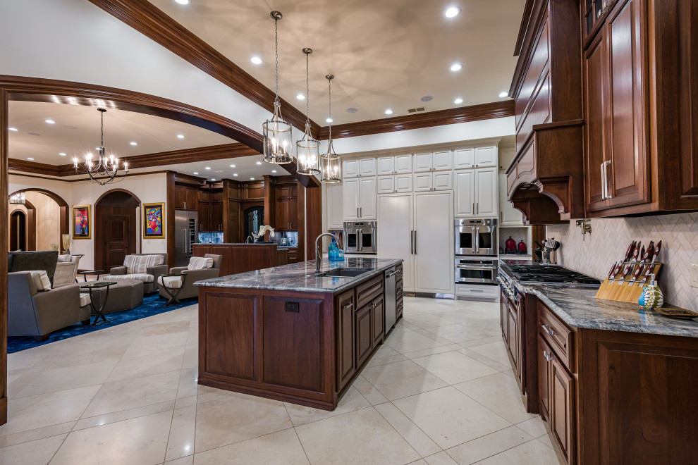 Photo of a large traditional l-shaped kitchen in Dallas with an undermount sink, raised-panel cabinets, dark wood cabinets, granite benchtops, beige splashback, travertine splashback, stainless steel appliances, travertine floors, with island, beige floor and grey benchtop.