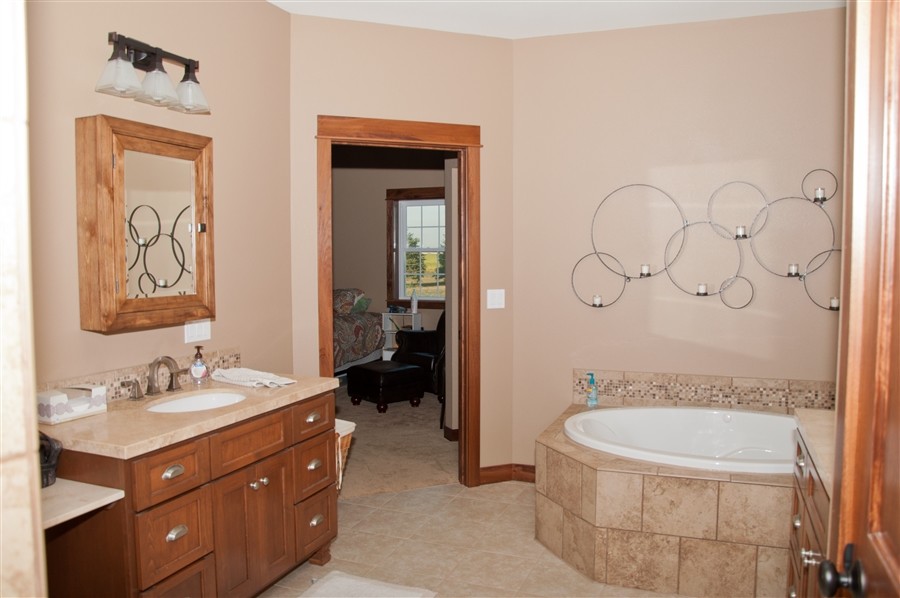 This is an example of a mid-sized arts and crafts master bathroom in Other with recessed-panel cabinets, medium wood cabinets, a drop-in tub, beige tile, beige walls, ceramic floors, an undermount sink, limestone benchtops and beige floor.