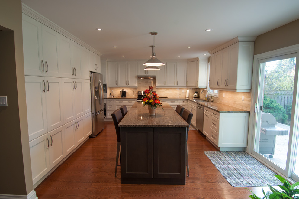 This is an example of a large transitional u-shaped separate kitchen in Toronto with shaker cabinets, white cabinets, granite benchtops, beige splashback, ceramic splashback, stainless steel appliances, with island, a double-bowl sink and medium hardwood floors.