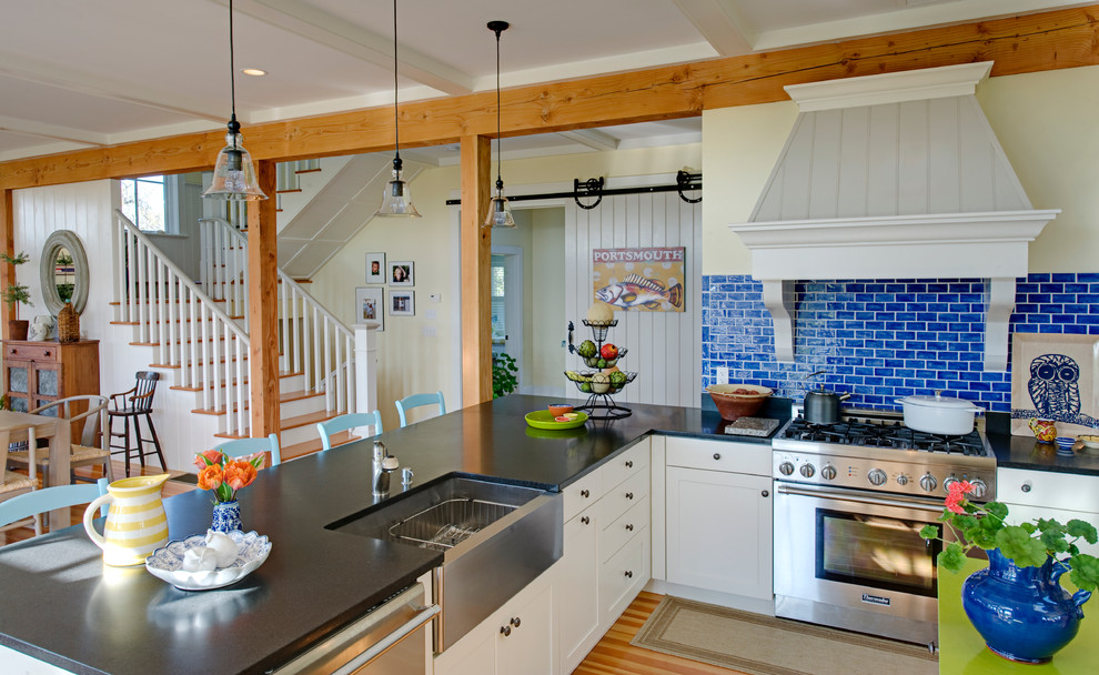 Inspiration for a beach style l-shaped open plan kitchen in Boston with a farmhouse sink, shaker cabinets, white cabinets, blue splashback, subway tile splashback, stainless steel appliances, light hardwood floors and a peninsula.